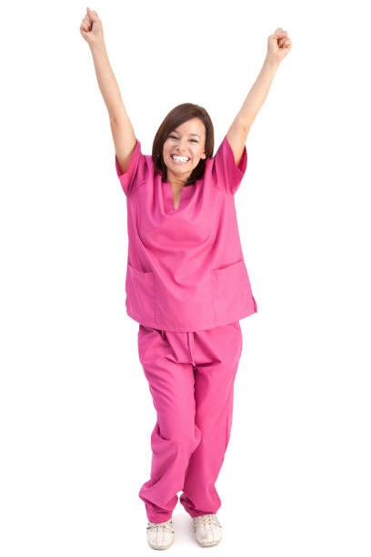Photo of an enthusiastic young nurse in pink scrubs, cheering with arms raised in the air; isolated on white.