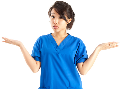 Young Asian female nurse in blue scrubs, shrugging with hands in the air as if uncertain or confused; isolated on white.
