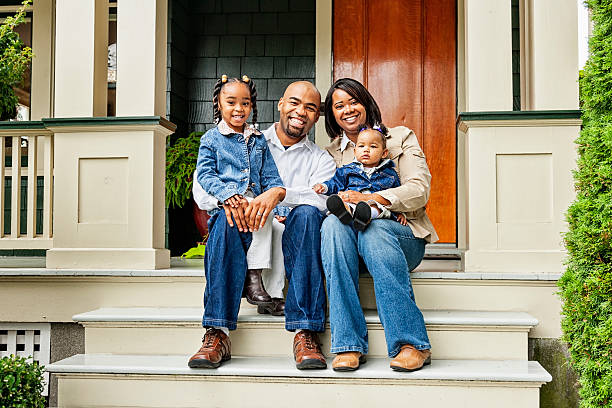 Happy Family on Front Porch Portrait of a young family sitting on the steps in front of their house. in front of photos stock pictures, royalty-free photos & images