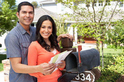 Hispanic Couple Checking Mailbox Holding Mail and Smiling at Camera