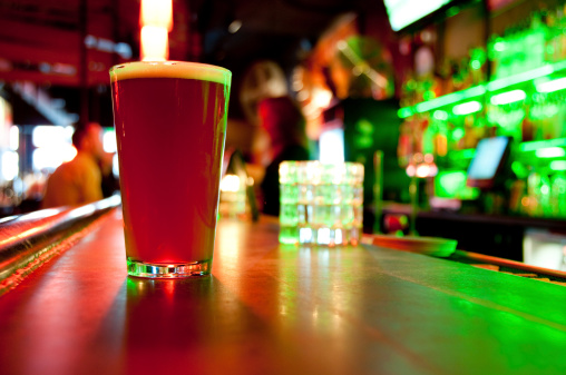 Glass of beer with a colorful neon background with unrecognizable people.