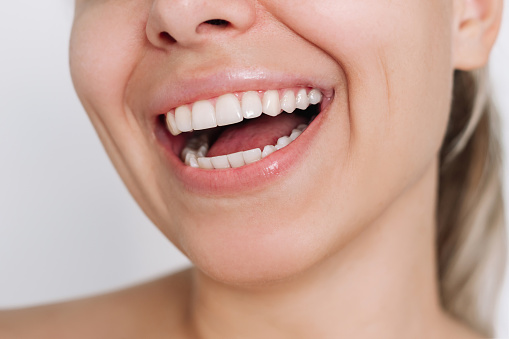 Cropped shot of a young caucasian blonde woman with perfect white even teeth on a white background. Oral hygiene, dental health care. Teeth whitening. Dentistry, beautiful smile