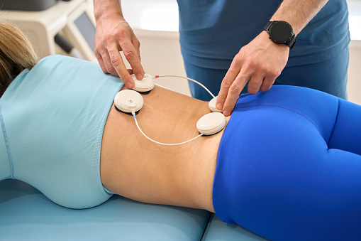 Male rehabilitation specialist putting sensors at female spine, conducting myostimulation procedure for rehabilitation after serious injuries and for sedentary patients