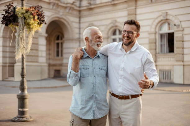 Happy Senior Father and Adult Son Walking and Talking Senior Father and Adult Son Walking and Talking Through the City Streets father son grandfather fathers day stock pictures, royalty-free photos & images