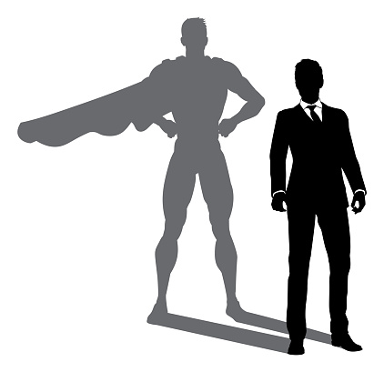 A superhero business man revealed by his shadow silhouette as a super hero in a cape
