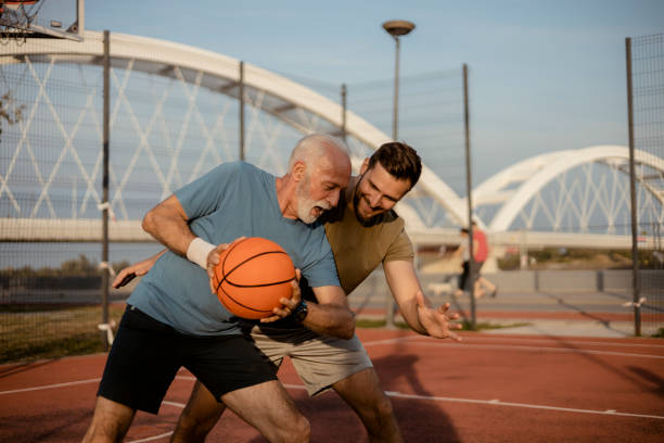 Basketball is a great way to bond Happy Senior Father and Adult Son Playing Basketball on a Court. Having Fun Together father son grandfather fathers day stock pictures, royalty-free photos & images