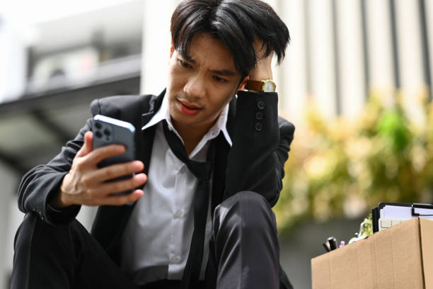 istock Sad, depressed businessman using smartphone in front of office center. Dismissal from work, unemployment concept 1684215196