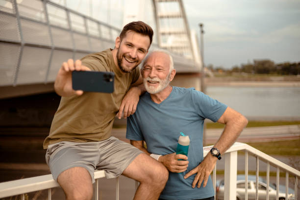 Adult Son and Active Senior Father Having Fun Together and Taking Selfie Adult Son and Active Senior Father Having Fun Together and Taking Selfie After Sports Training father son grandfather fathers day stock pictures, royalty-free photos & images