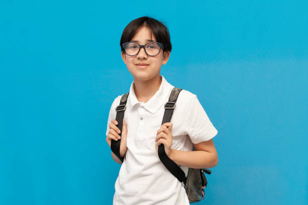 niño asiático escolar de doce años con gafas y con sonrisas de mochila sobre fondo azul aislado - 10 11 years little boys child happiness fotografías e imágenes de stock