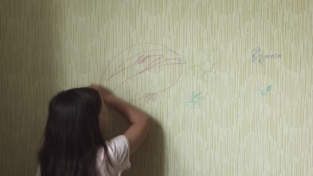 Black haired little girl draw doodle with purple marker on old wallpaper back view, develop artistic skills. Space for painting, disorderly conduct, drawing, paperhanging damage, scribble