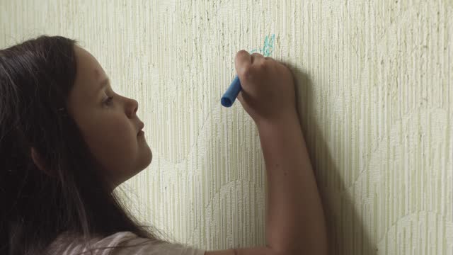 Little girl diligently draw animal with blue marker on wallpaper side view closeup, practice artistic skills. Space for painting, disorderly conduct, drawing, paperhanging damage, childish fantasy