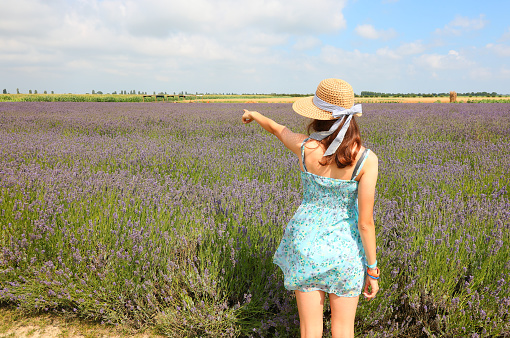 young girl wearing summer dress and straw hat in lavender flower field in the countryside in summer