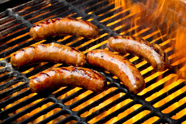 bratwurst หรือฮอทดอกบนตะแกรงพร้อมเปลวไฟ - ปิ้งย่าง ภาพสต็อก ภาพถ่ายและรูปภาพปลอดค่าลิขสิทธิ์