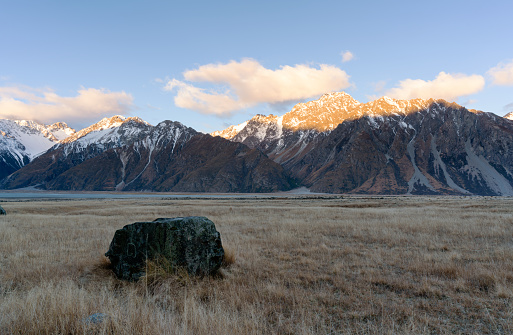 A large boulder, known as an erratic, which has been deposited by an ancient glacier. In the distance we see the snowcapped peaks of New Zealand's Southern Alps.
