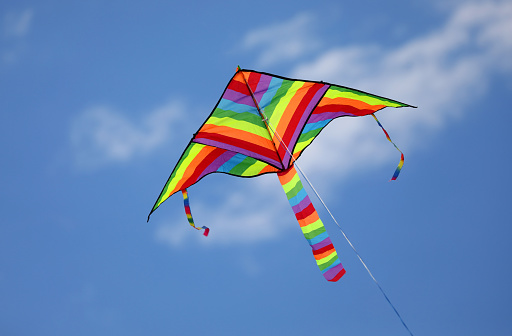 toy kite with rainbow hues flies tied on a string in the sky