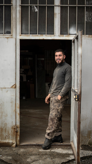 carpenter man stands at the door of the workshop and smiles