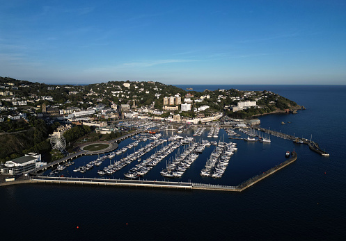 This high angle view of the seaside resort of Torquay shows yachts and motorboats moored inside of the Marina as well as the Princess Theatre (far left), the English Riviera Wheel (next to the Theatre) and properties and hotels stretching around to Babbacombe (far right). Torquay is a popular UK holiday resort during the summer months. The marina has numerous attractions including pubs, bars, restaurants and shops. The marina itself is a haven for boats, yachts, trawlers and tourist boats.