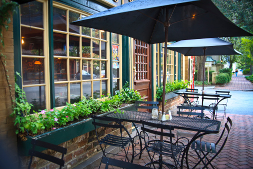 Cozy and picturesque street cafe  (bistro) with window boxes, chairs, tables and umbrellas. Brick sidewalk, French windows and front door. City life; cafe society; small restaurant; Savannah, Georgia.
