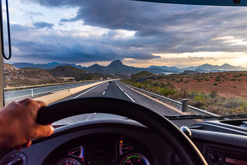 View from the driving position of a truck of the highway and a landscape of mountains in the background at dawn.