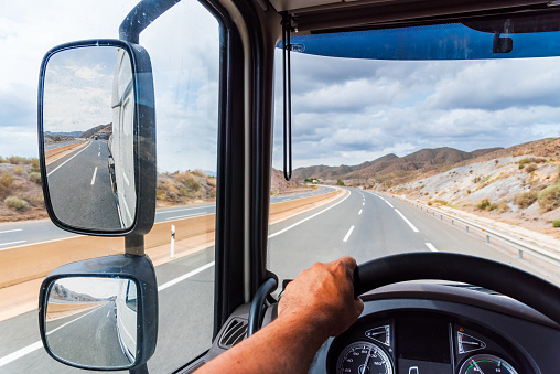 View from the driving position of a truck of the rearview mirror and the empty highway.