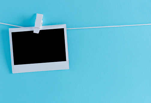 Blank photo on a clothesline, blue background. Polaroid.