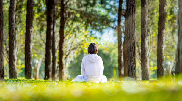 frau praktiziert entspannend meditation im kiefernwald, um glück aus innerem frieden zu erlangen weisheit mit sonnenstrahl licht für gesunden geist und seele konzept für gesunden geist und seele - nirvana stock-fotos und bilder