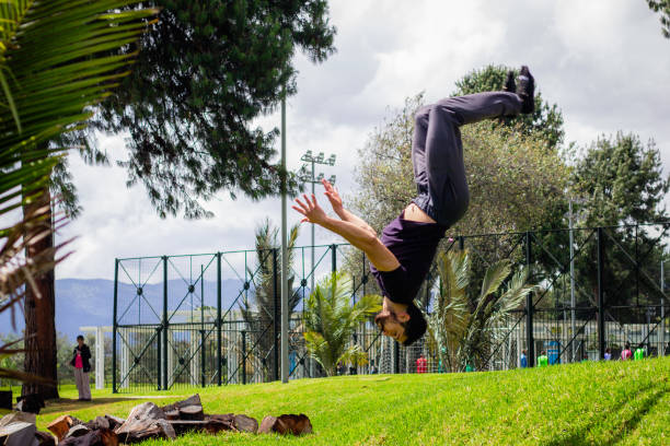 young man doing a back flip in a park, practicing gymnastics outdoors