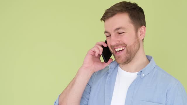 Young cheerful smiling happy man talking on mobile cell phone isolated on olive background.