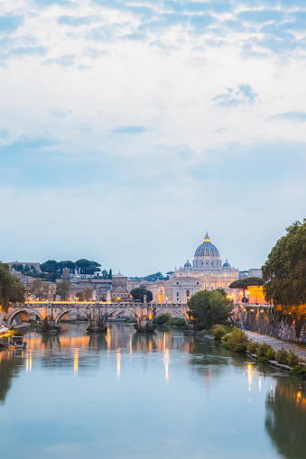 Scenic twilight view of Saint Peter's Basilica at Vatican City and Ponte Vittorio Emanuele II illuminated along the Tiber River on a summer evening in Rome, Italy.