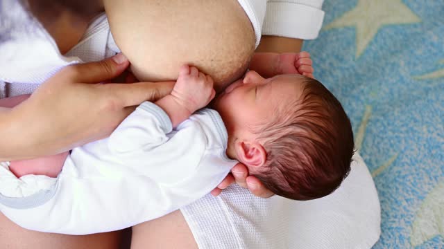 Overhead view. Adorable newborn baby sucking mother's breast. Close-up conscious loving mother breastfeeding her baby
