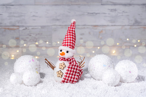 Decorative snowman on the snow is decorated with a snowball. Christmas and New Year decor. White bokeh background.