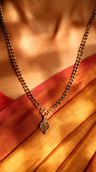 A closeup shot of a gold necklace with black beads and a pendant around a woman's neck