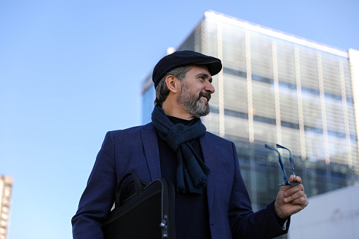 Middle-aged businessman with a cap on his head in front of an office building