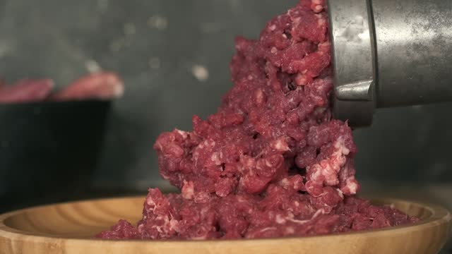 Close up of mincing beef meat with old manual meat grinder. Cooking meat for hamburger patties. Black concrete background