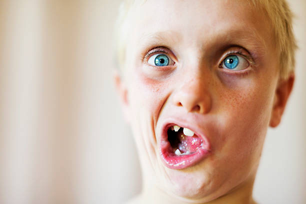 Cute blond 8 year old boy makes zany face Fooling around, this cute blond, blue-eyed 8 year old makes a squinting, toothy grimace. ignorance photos stock pictures, royalty-free photos & images