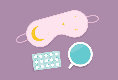 Eye mask, cup, and sleeping pills on a table for insomnia concept