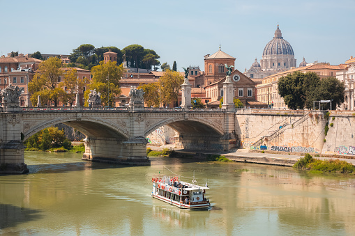 Scenic view on a sunny summer day of a tourist boat cruise along the Tiber River past Saint Peter's Basilica, Vatican City and Ponte Vittorio Emanuele II.