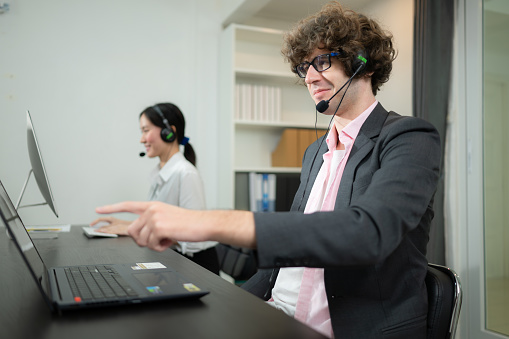 Group of business people wearing headset working actively in office. Call center, telemarketing, customer support agent provide service on telephone video conference call.