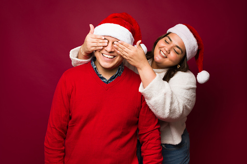 Happy fat woman surprising a latin man covering his eyes and giving him a surprise christmas present