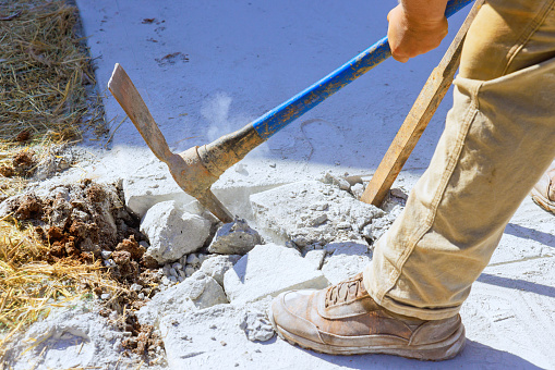 Worker smashes concrete old driveway with pickaxe on construction site