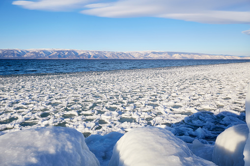 Winter landscape. Snow and ice floes near the shore, open water in the unfrozen Lake Baikal in December.