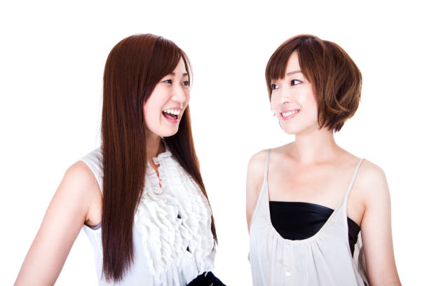 Two beautiful young Japanese brunette women standing and talking with one another against a white background in studio.
