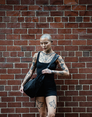 Street portrait of a young, beautiful bald woman with many tattoos. Perfect beige skin,  passionate girl with informal strange appearance. New York City, USA