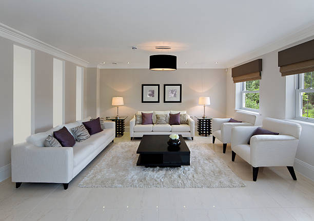 beautiful family room a large and spacious family room in an exclusive new house that has been tastefully furnished in a contemporary style. Seating comprises a large four seater and three seater settee together with two matching armchairs, all facing a large modern coffee table on a cream coloured rug. Purple and light brown silk cushions add some subtle colours. On the left, three large opaque panels allow light from an adjecent hallway to come through. The lights have also been turned on to add some warmth to this scene. Copyright for the artwork on the wall belongs to the photographer. architectural cornice stock pictures, royalty-free photos & images