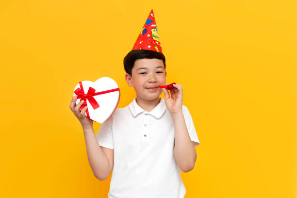 niño asiático de diez años con sombrero de fiesta con regalo celebra cumpleaños sobre fondo amarillo aislado - 10 11 years little boys child happiness fotografías e imágenes de stock