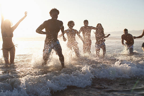 gruppe junger freunde spielen in den wellen am strand - wading stock-fotos und bilder