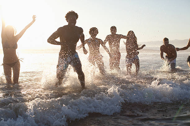 グループの若い友人がビーチで遊ぶウェイブズ - 水につかる ストックフォトと画像