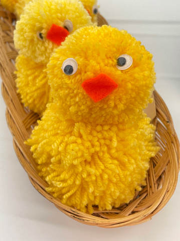 Stock photo showing close-up, elevated view of a set of three woollen chicks made from yellow pom-poms with orange felt beaks and googly eyes made for group of woollen toys entry to a village show handicraft competition.