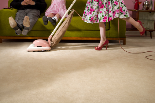 housewife hoovers under the family trying to keep her copy space clean