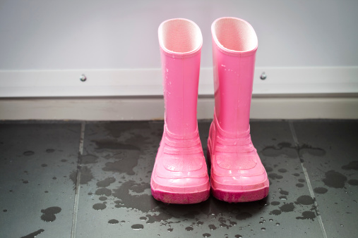 A pair of wet  pink  galoshes in the entrance way.